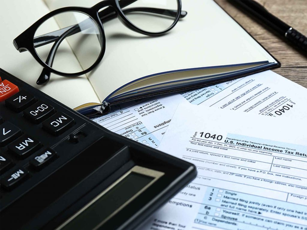 Pile of tax forms for expats on a desk. With calculator, notebook and eyeglasses.