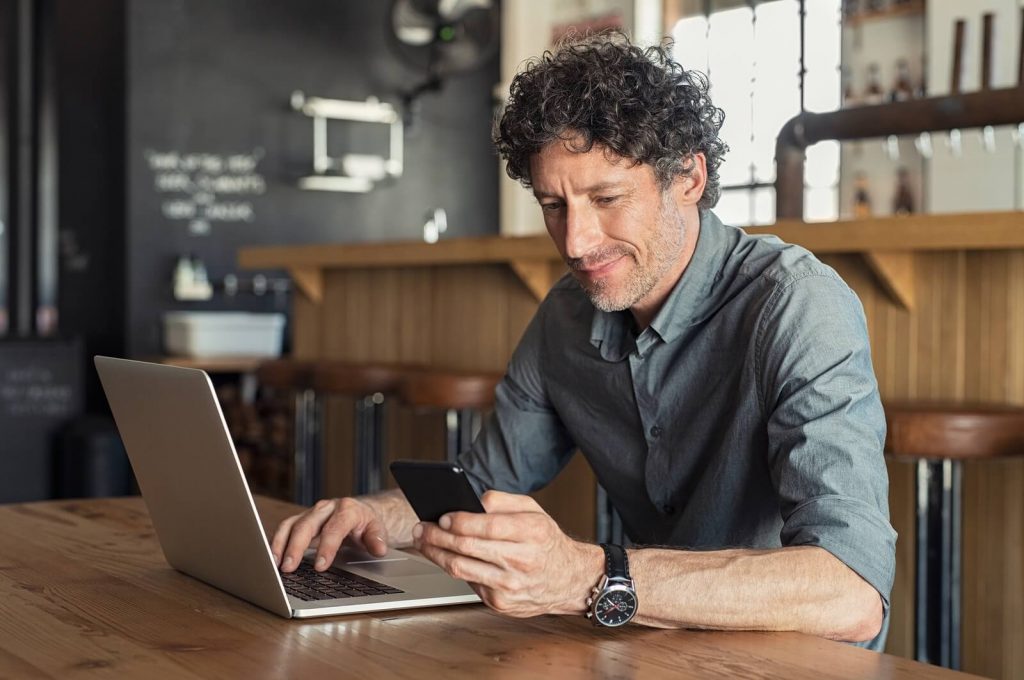 Happy mature business man sitting at a cafe with his laptop filing US expat taxes.