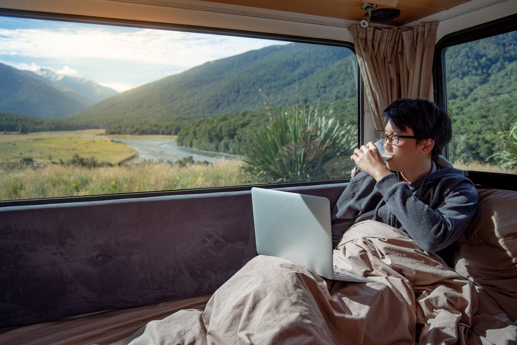 A digital nomad drinks a latte while sitting in his Van-Life van.