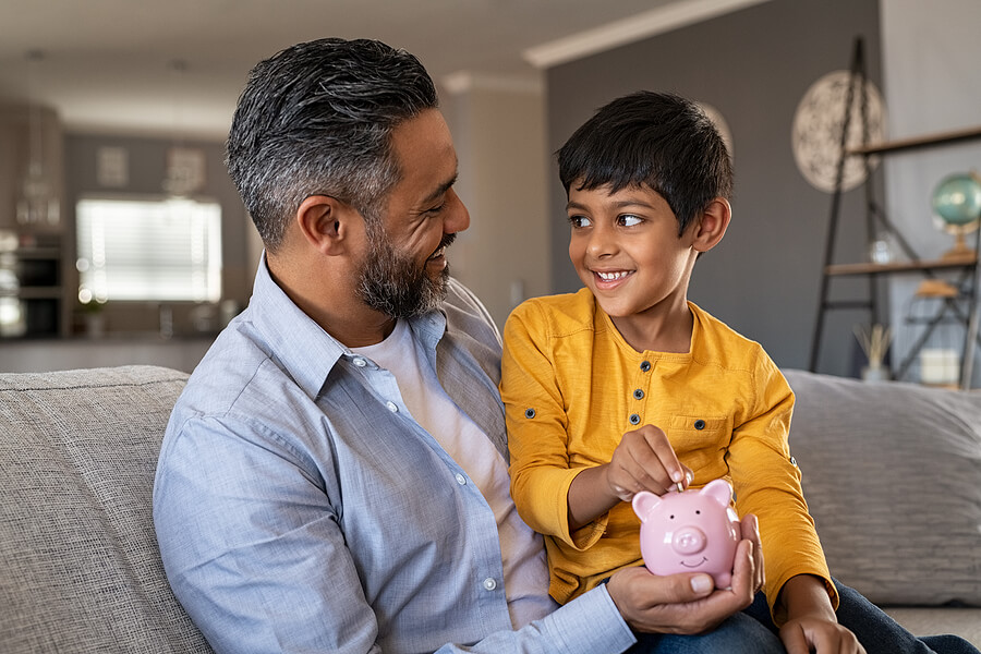 Father and son putting money and in a piggy bank. Saving as expats thanks to the child and dependent care credit.