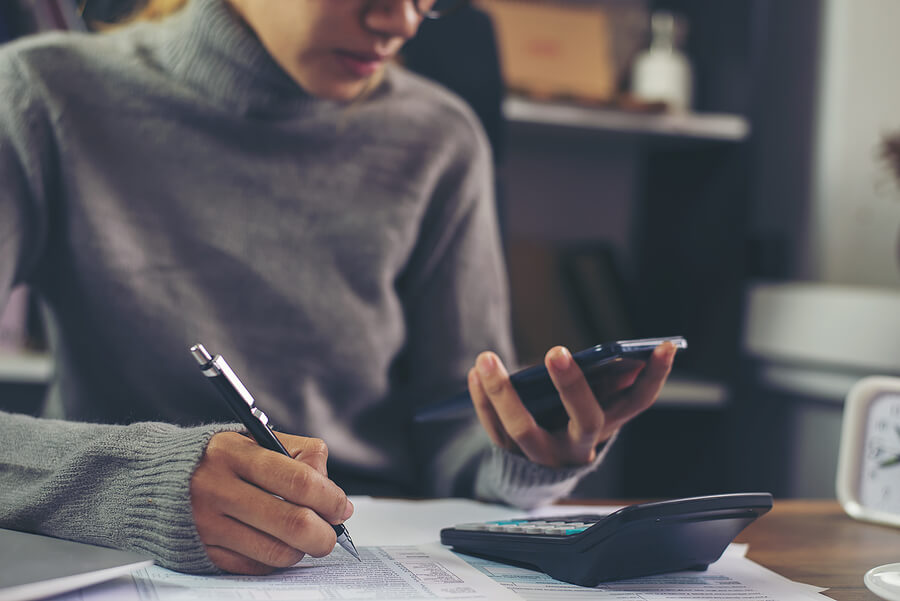 Expat woman holding phone with her 1040 tax form and a calculater on the desk. She is wondering "do I owe US taxes?"